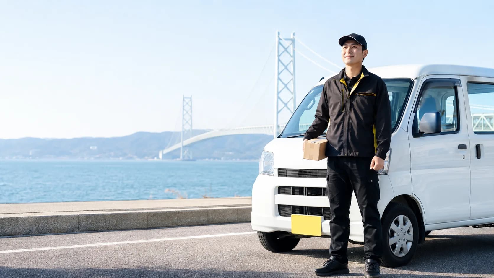 明石海峡大橋を背に、軽貨物車両の前に立つJUNGLE TRANSPORTの配送ドライバー